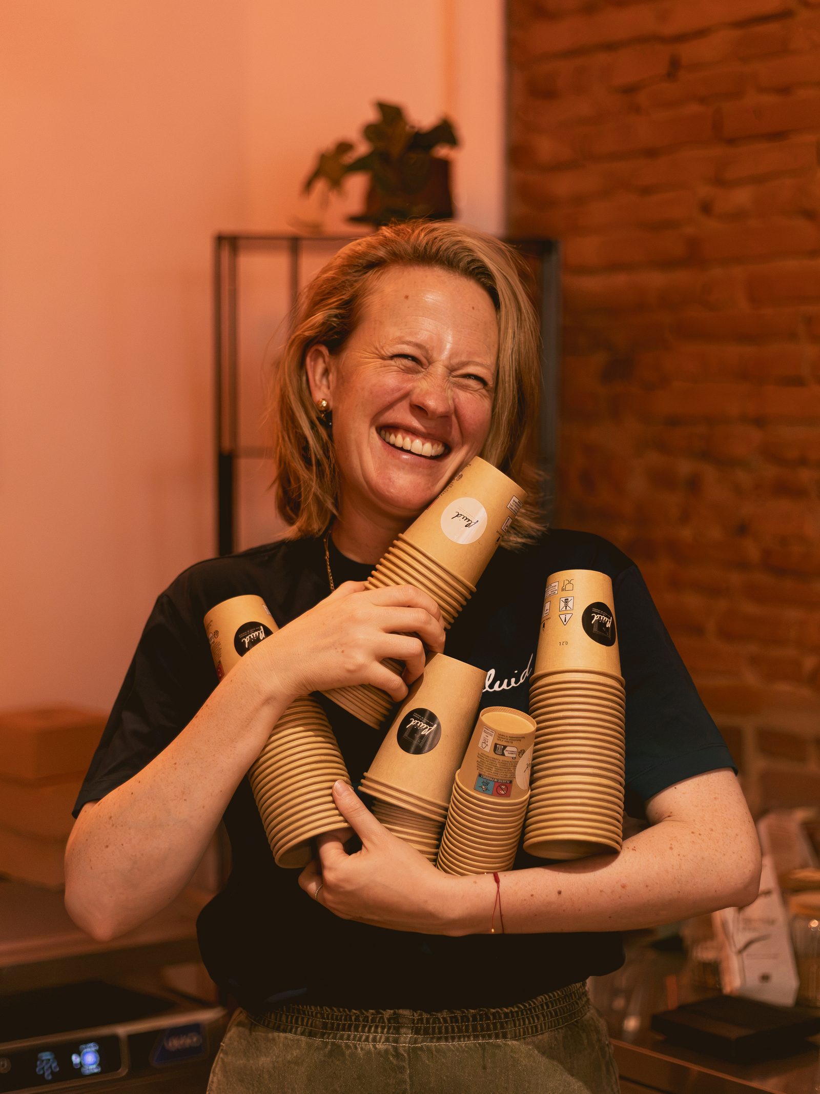 Adélaïde éclate de rire, les bras chargés de gobelets Fluid