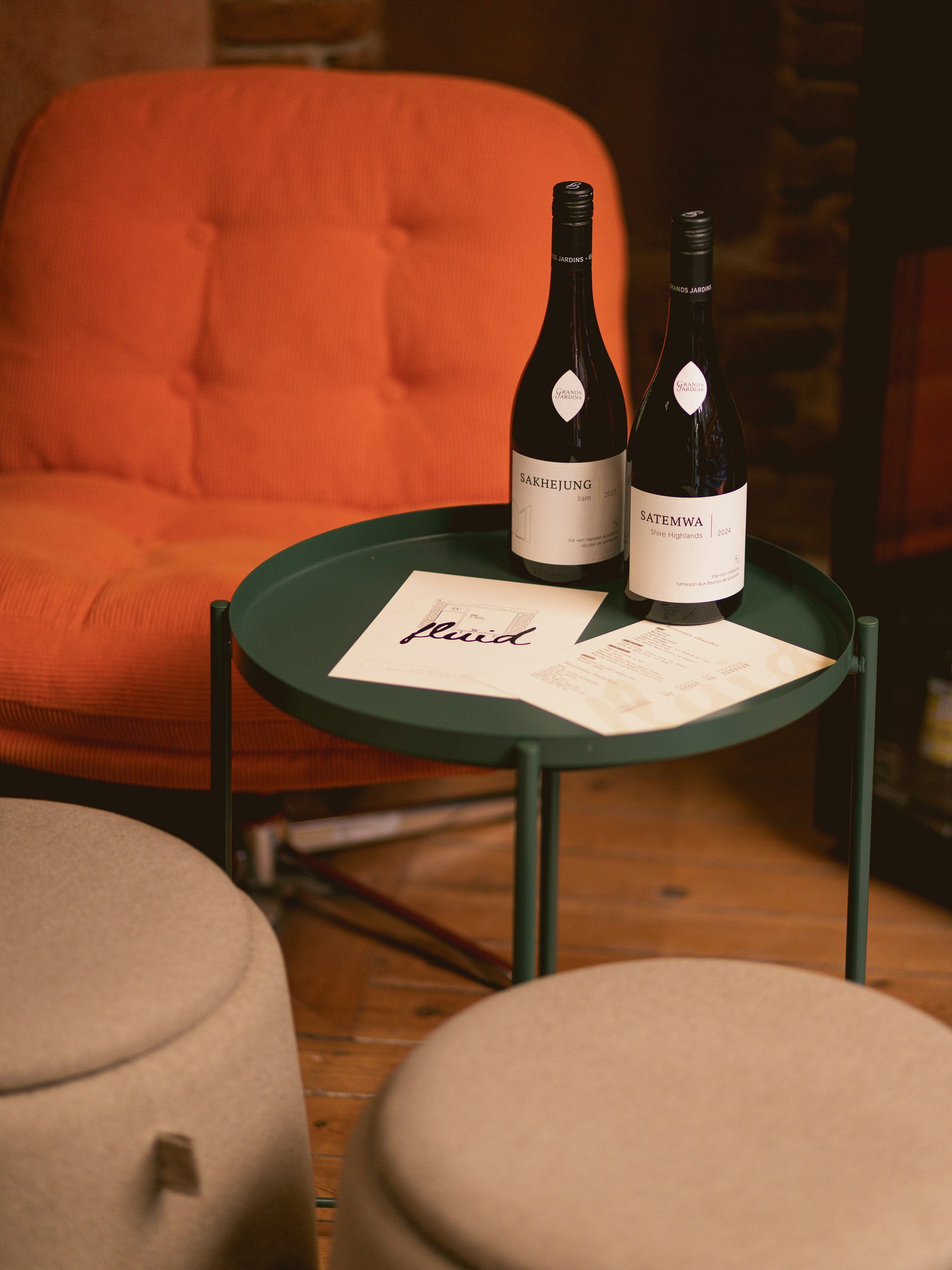 Deux bouteilles Grands Jardins sur la table verte devant le fauteuil orange